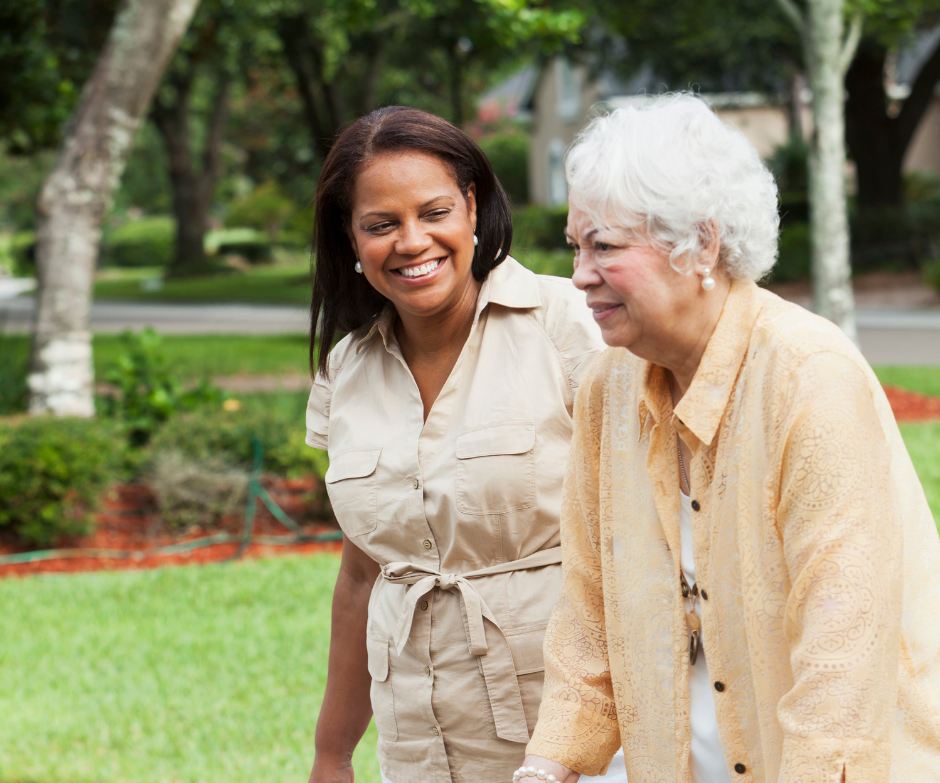A caregiver sitting close to an older client on her sofa at home, both smiling