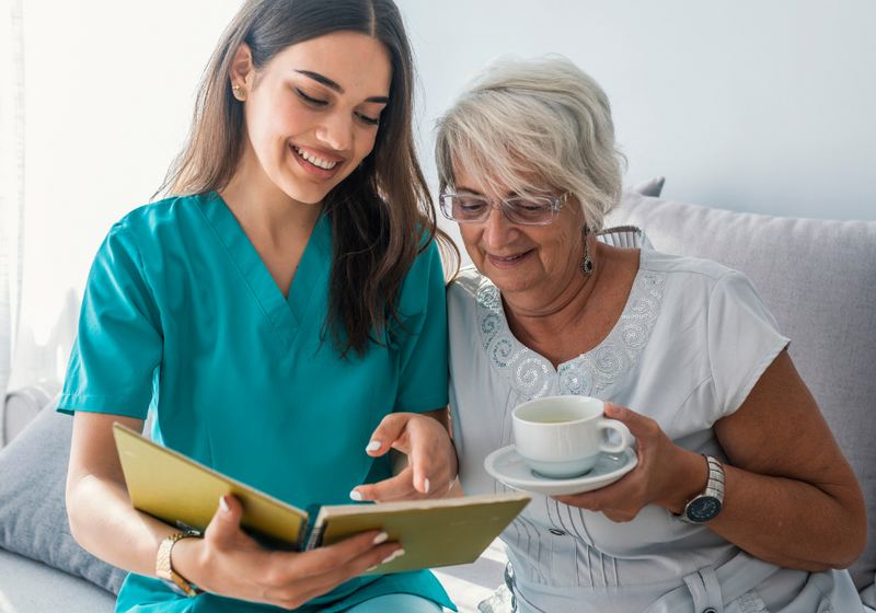 A caregiver reading a book together with an older woman having tea